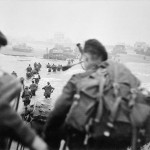 The British 2nd Army  on 'Queen Red' Beach, the Sword Area at approximately 8:40 a.m. Brigade commander,  Lord Lovat, can be seen striding through the water to the right of the column of men. The figure nearest the camera is bagpiper, Bill Millin. (June 6, 1944). Source: Imperial War Museums,  B 5103.
