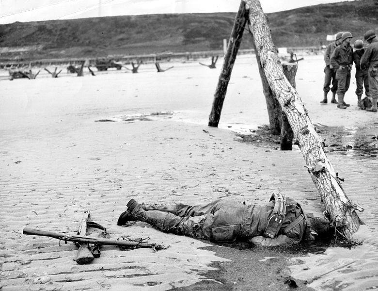 An American Soldier lies dead alongside an anti-landing craft obstruction on Omaha Beach. (June 6, 1944). Source: U.S. National Archives, # 26-G-2397.
