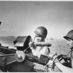 2 Ohio Coast Guardsmen (John R. Smith, on the left, and Daniel J. Kaczorowski) stand at their guns aboard a Coast Guard-manned invasion transport during the invasion of Normandy. Source: U.S. National Archives, 513179.