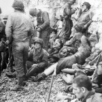 American troops of the 3d Battalion, 16th Infantry Regiment, 1st U.S. Infantry Division, after gaining safety by the chalk cliff at their backs. They take a "breather" on Omaha Beach. (June 8, 1944). Source: U.S. National Archives, # 26-G-2342.