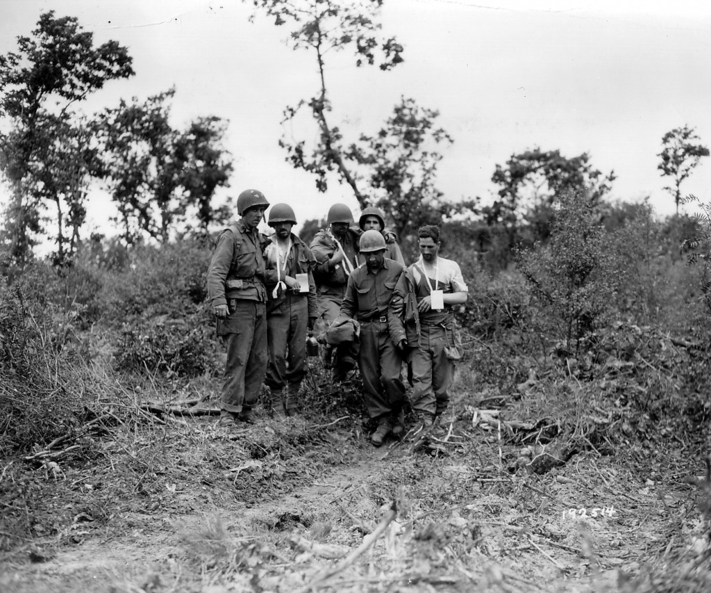 Soldiers on the outskirts of the Haye du Puits in the area of farmland back down their wounded. (July 7, 1944). Source: Archives Normandie 39-45 #013885.