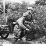 Two German paratroopers with handcarts loaded with equipment running through bushes. Normandy, France. (June 21, 1944). Source: German Federal Archive, Bild 101I-587-2253-05.