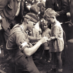Canadian Private MacDonald gives first aid to a child. (1944). Source: Ken Bell.