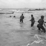 U.S. troops rescue men from a sunken landing craft on D-Day. (June 6, 1944). Source: U.S. National Archives, # SC 320869.