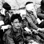 Wounded U.S. troops of the 3rd Battalion, 16th Infantry Regiment, 1st U.S. Infantry Division, receive cigarettes and food after they stormed Omaha Beach. Colleville-sur-Mer, Normandy, France. (June 6, 1944). Source: U.S. National Archives, SC 189910-S.