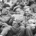 Final Embarkation: 3 British soldiers of 51st Highland Division in a landing craft pass the time by reading a booklet on France which they were issued before embarkation. (June 6, 1944). Source: Imperial War Museums,  B 5207.