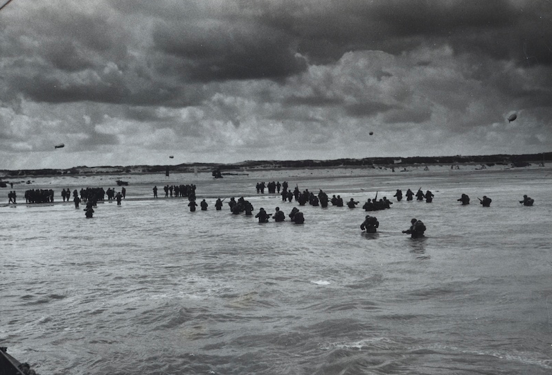 Waist deep in the surf, American reinforcements pour ashore from landing barges replacing earlier troops in the liberation waves and spreading inland through Normandy. Source: U.S. National Archives, # 26-G-2412.