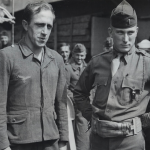 Nazi prisoner on the left was a Brooklyn butcher for 10 years before returning to Germany to fight for Hitler. Captured in Normandy, a Coast Guard-manned transport carries him back to the U.S. for internment. Source: U.S. National Archives, # 26-G-2579.