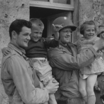 Shortly after the landings on the French coast, two Yanks make friends with the younger locals in France.  (June 9, 1944). Source: U.S. National Archives, # 111-SC-190066.