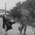 G.I. of the 82nd Airborne Division helps a French woman carry her belongings back to Eglise Sur-Mer, Utah Beach, France. The village was evacuated during the Normandy invasion. (June 8, 1944). Source: U.S. National Archives, # 111-SC-190287.