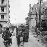 A jeep and other vehicles and troops passing through La Breche as they move inland from Sword Beach, Normandy. (June 6, 1944). Source: Imperial War Museums, B 5036.