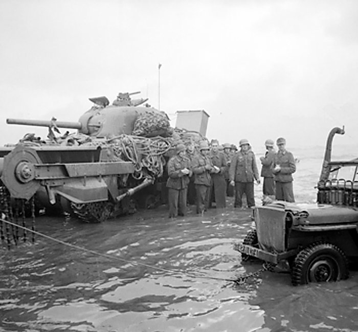 German prisoners awaiting transfer at the beaches of Normandy, France. A disabled Sherman Crab flail tank in background. (June 6, 1944). Source: Imperial War Museums, #4700-29 B 5089, Photographer:  J. Mapham.
