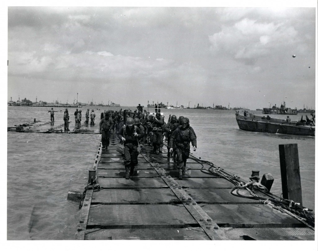 Soldiers coming ashore on a pontoon causeway built by the SeaBees. This causeway was laid down at Omaha Beach during the Normandy Invasion. Source: U.S. National Archives, # 6682629.