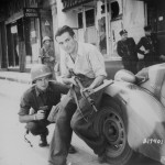 An American officer and a French partisan crouch behind an auto during a street fight in a French city. (1944). Source: U.S. National Archives, # 111-SC-217401.